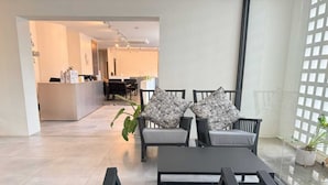 A modern living room with a sofa set, a coffee table, and a dining area in the background. - Collection O The Singha Chiangmai Hotel (Chiang Mai)