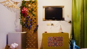 Una habitación con un armario de madera, una mesita con un azulejo decorativo, un televisor montado en la pared y una cortina verde.