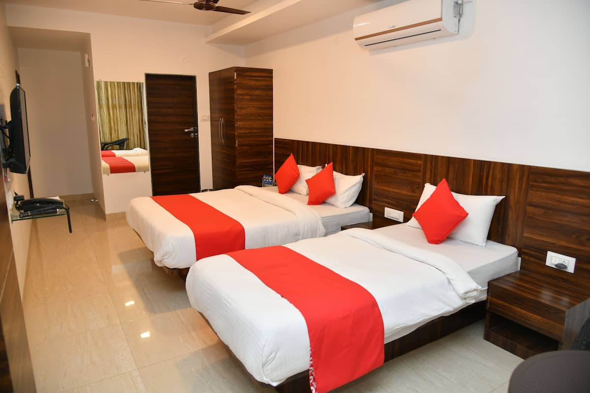 A hotel room with three beds, each with red and white bedding, a wooden headboard, and a small wooden nightstand.