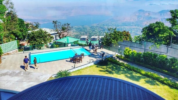 A pool area with a view of distant mountains, outdoor seating, and a fenced garden. - Hotel Royal Orbit (Jaoli)