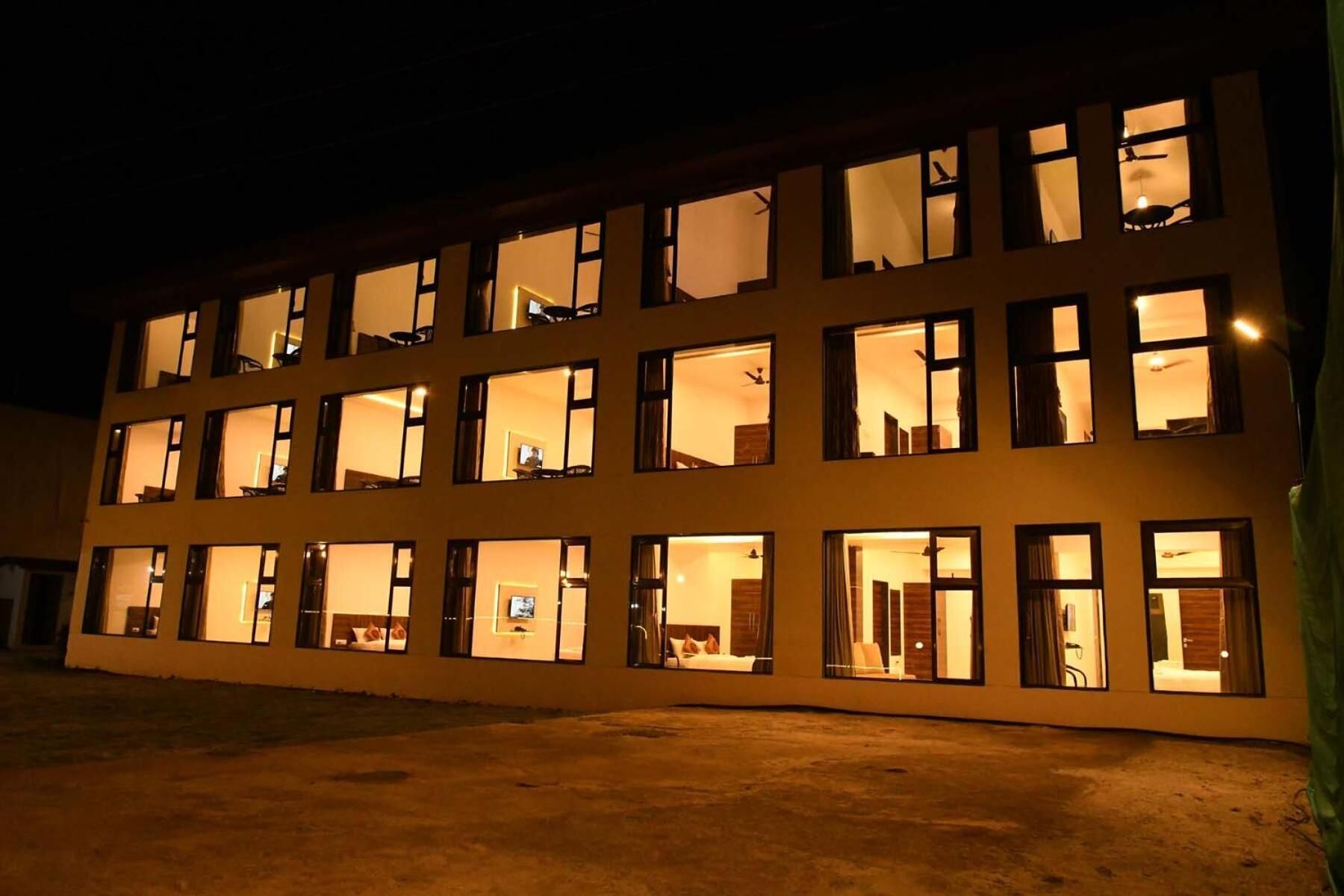 Un hotel de varios pisos con ventanas iluminadas, techo plano y base de concreto.