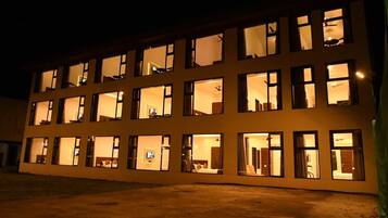 Un hotel de varios pisos con ventanas iluminadas, techo plano y base de concreto.