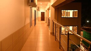 A corridor with tiled flooring, a metal railing, and an air conditioning unit on the wall. - Hotel Royal Orbit (Jaoli)