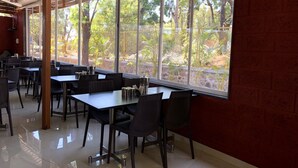 A restaurant with large windows, tables, and chairs. - Hotel Royal Orbit (Jaoli)