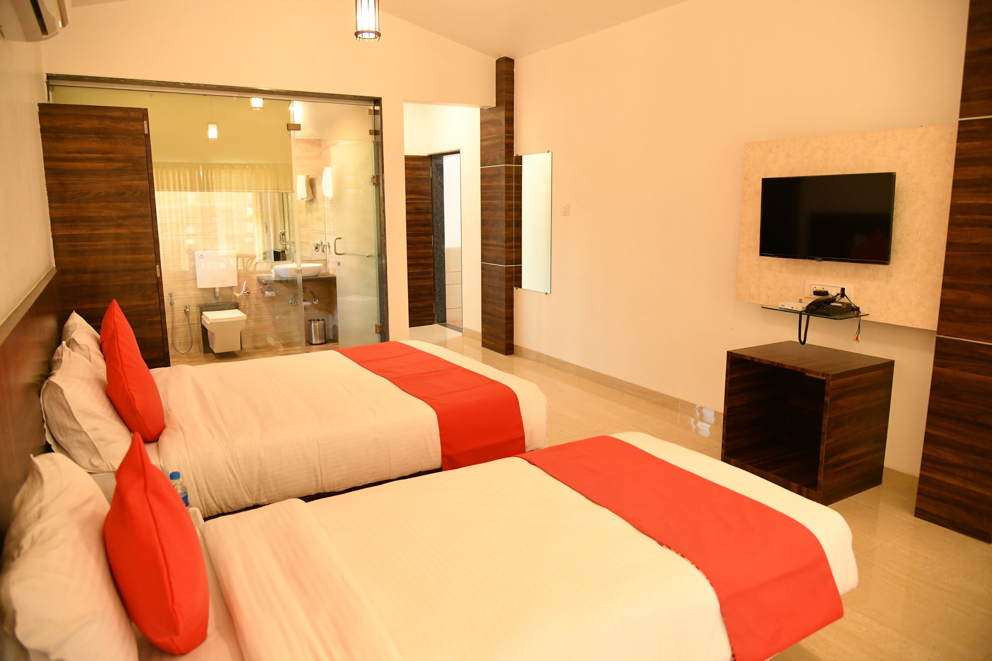 Habitación de hotel con dos camas, un televisor, un espejo y un baño visible a través de un vidrio.