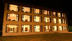 A multi-story building with multiple windows, each illuminated from the inside, suggesting interior lighting. - Hotel Royal Orbit (Jaoli)