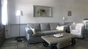 Un salón con un sofá gris, una mesa de centro de madera, un sillón blanco y un espejo en la pared.