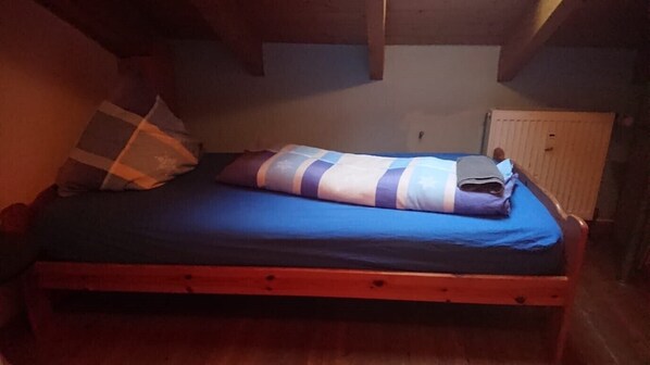 Una cama individual con colchón azul y manta a rayas, cabecero de madera y un radiador en la pared.