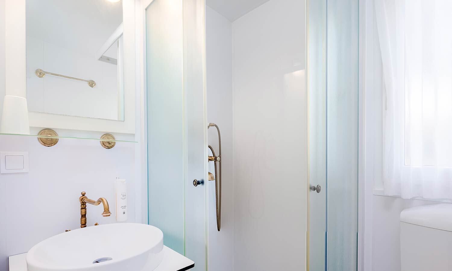A modern bathroom with a glass shower enclosure, a white sink with a gold faucet, and a mirror above the sink.