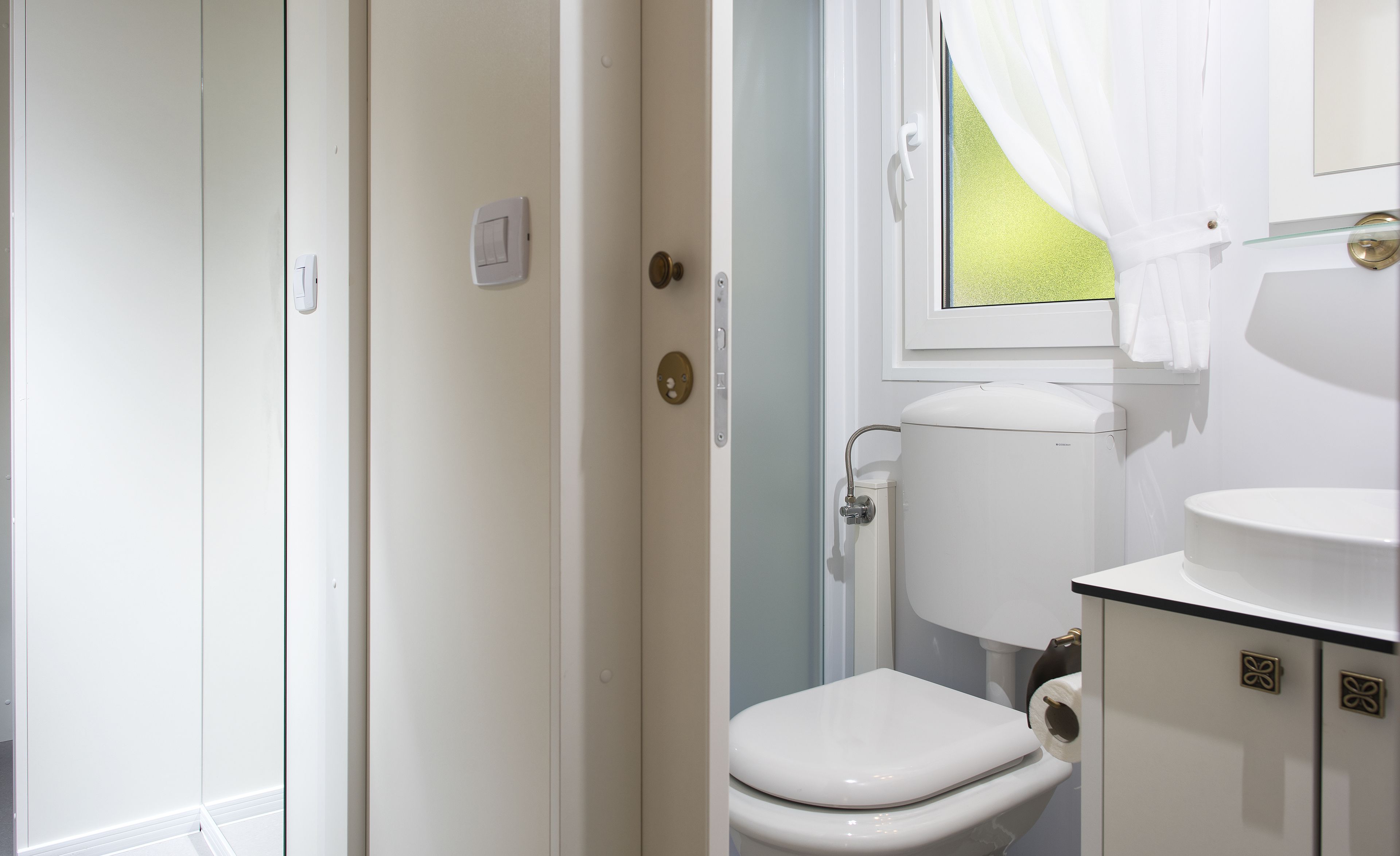 A bathroom with a toilet, a sink, and a window with curtains.