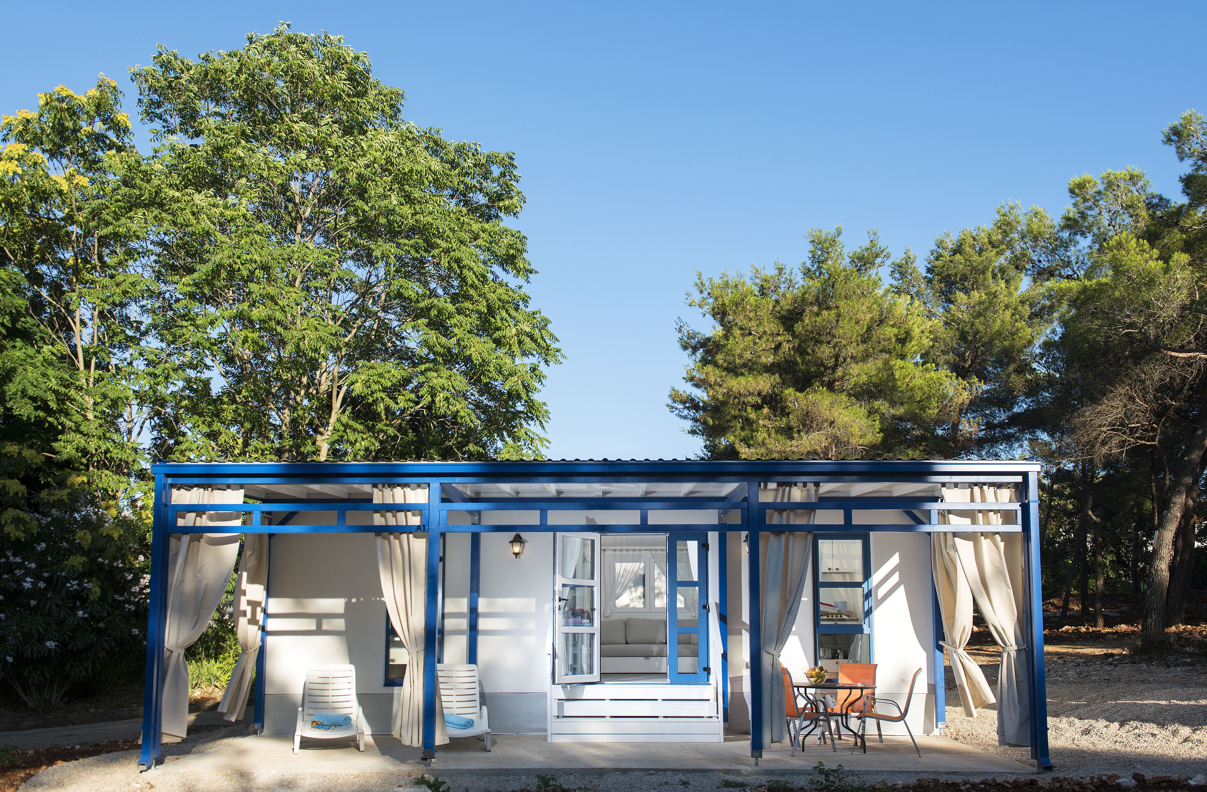 A small, single-story structure with a blue frame, a covered porch, and a seating area with a table and chairs.
