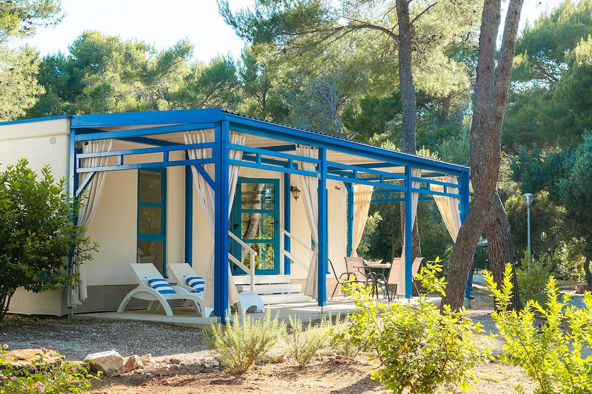 A small, single-story building with a blue and beige color scheme, featuring a covered outdoor seating area with chairs and a table.