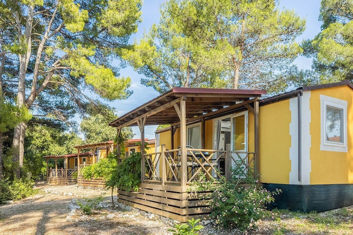 A row of small, yellow cabins with wooden decks and a covered porch, surrounded by trees.