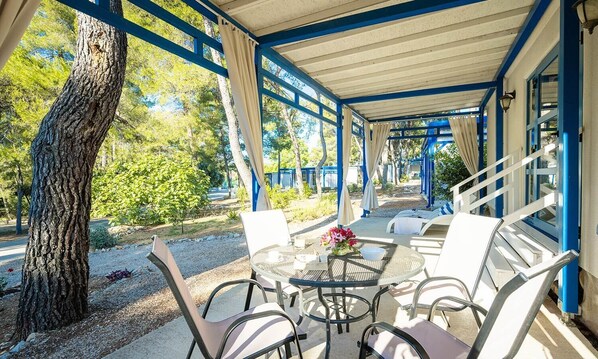 Un espace extérieur abrité, avec une table et des chaises, entouré d’arbres et offrant une vue sur le paysage.