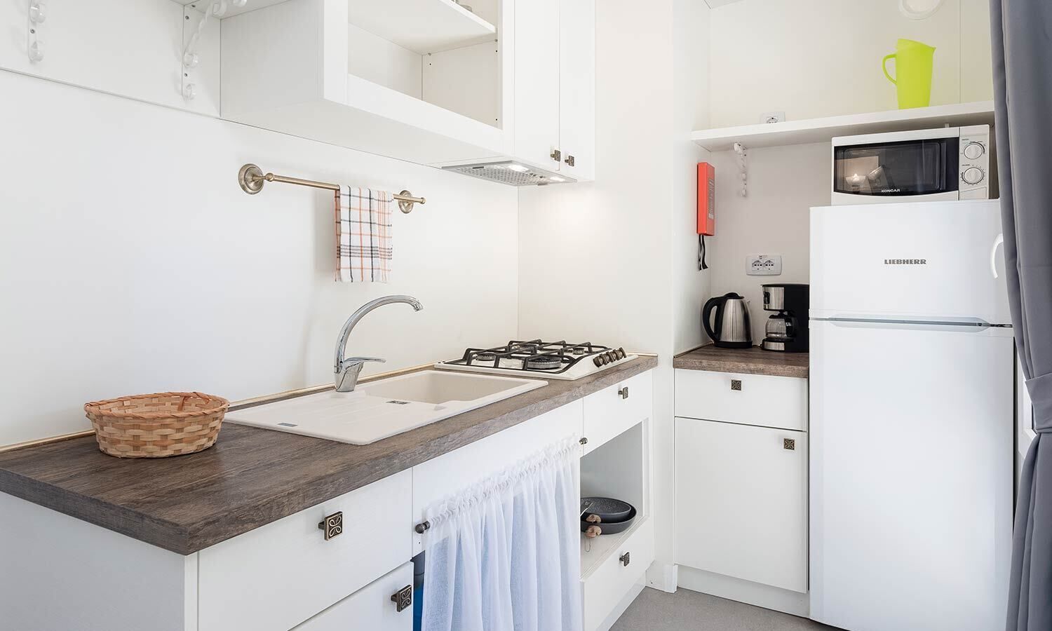 A modern kitchen with a sink, stove, and microwave. There is a basket on the counter and a towel hanging on the door.