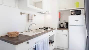 A modern kitchen with a sink, stove, and microwave. There is a basket on the counter and a towel hanging on the door.