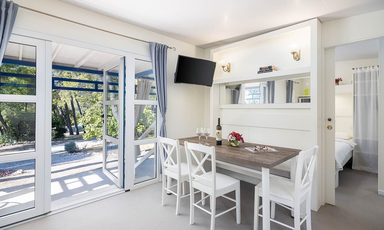Une pièce moderne comprenant une table et des chaises, un téléviseur à écran plat fixé au mur et une grande porte-fenêtre coulissante donnant sur un espace extérieur.