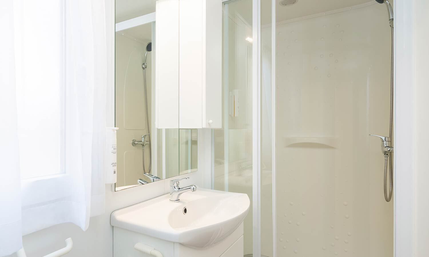 A modern bathroom with a white sink, a glass shower enclosure, and a large mirror.