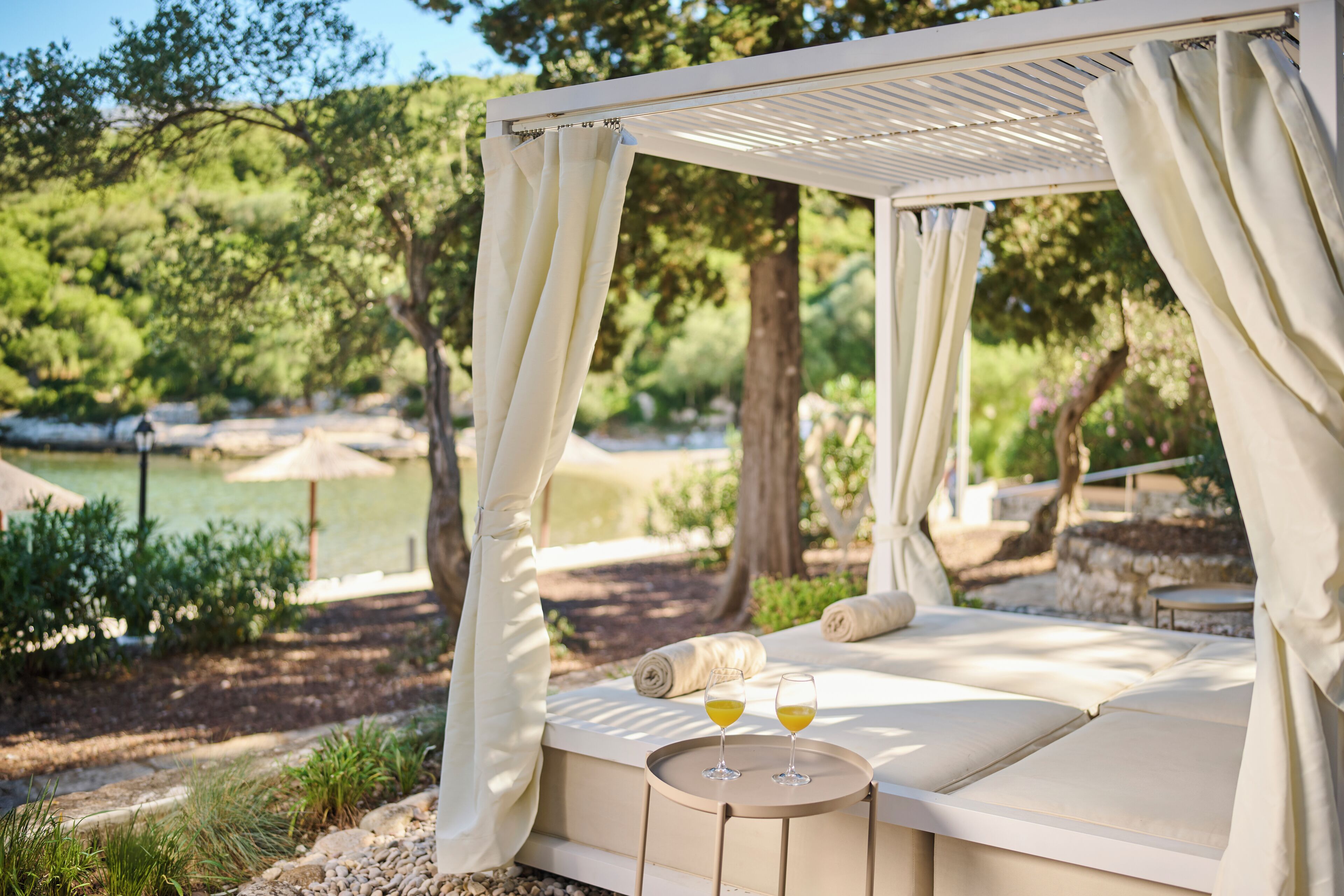 A cozy outdoor seating area with a canopy, a cushioned bench, and two glasses of orange juice on a small table.