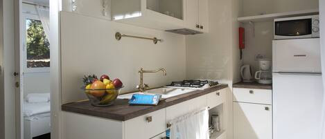 Una cocina funcional con estufa a gas, pileta y microondas. Hay un frutero en la encimera y un ventanal con cortinas.