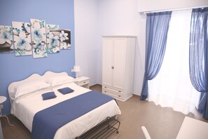 Ein Schlafzimmer mit Bett, weißem Wandschrank und blauen Vorhängen.