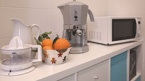 A kitchen counter with a juicer, a coffee maker, a microwave, and a bowl of oranges. - B&B La Baia Di Partenope (Naples)