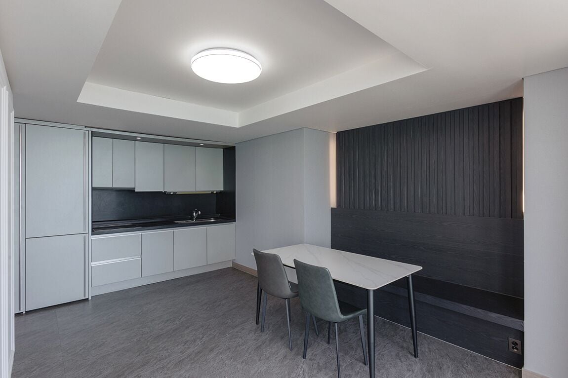 A modern kitchen with white cabinets, a black countertop, and a dining area with a white table and two chairs.