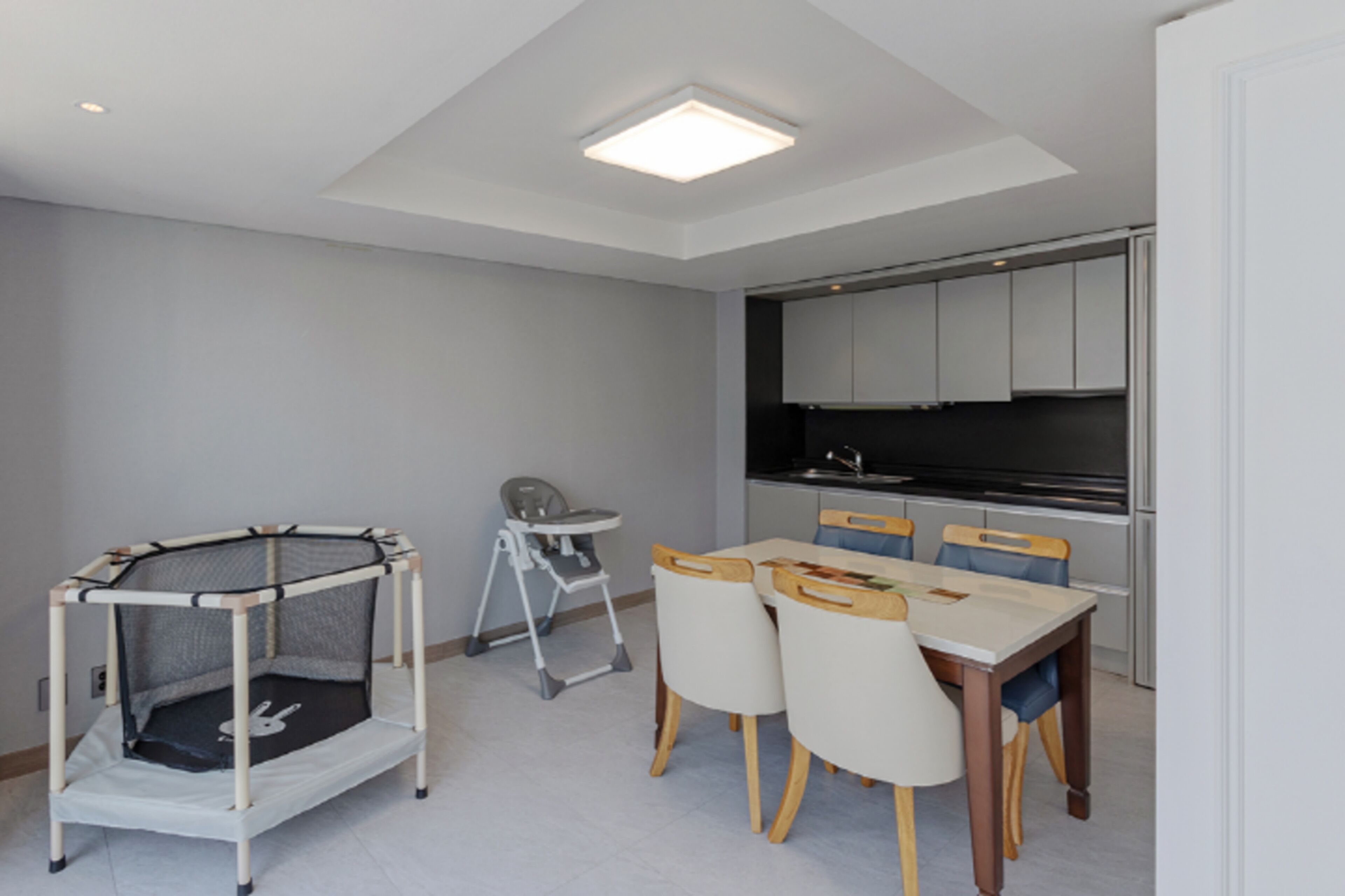 Cocina compacta con electrodomésticos modernos, comedor con mesa y sillas, y corralito para niños.