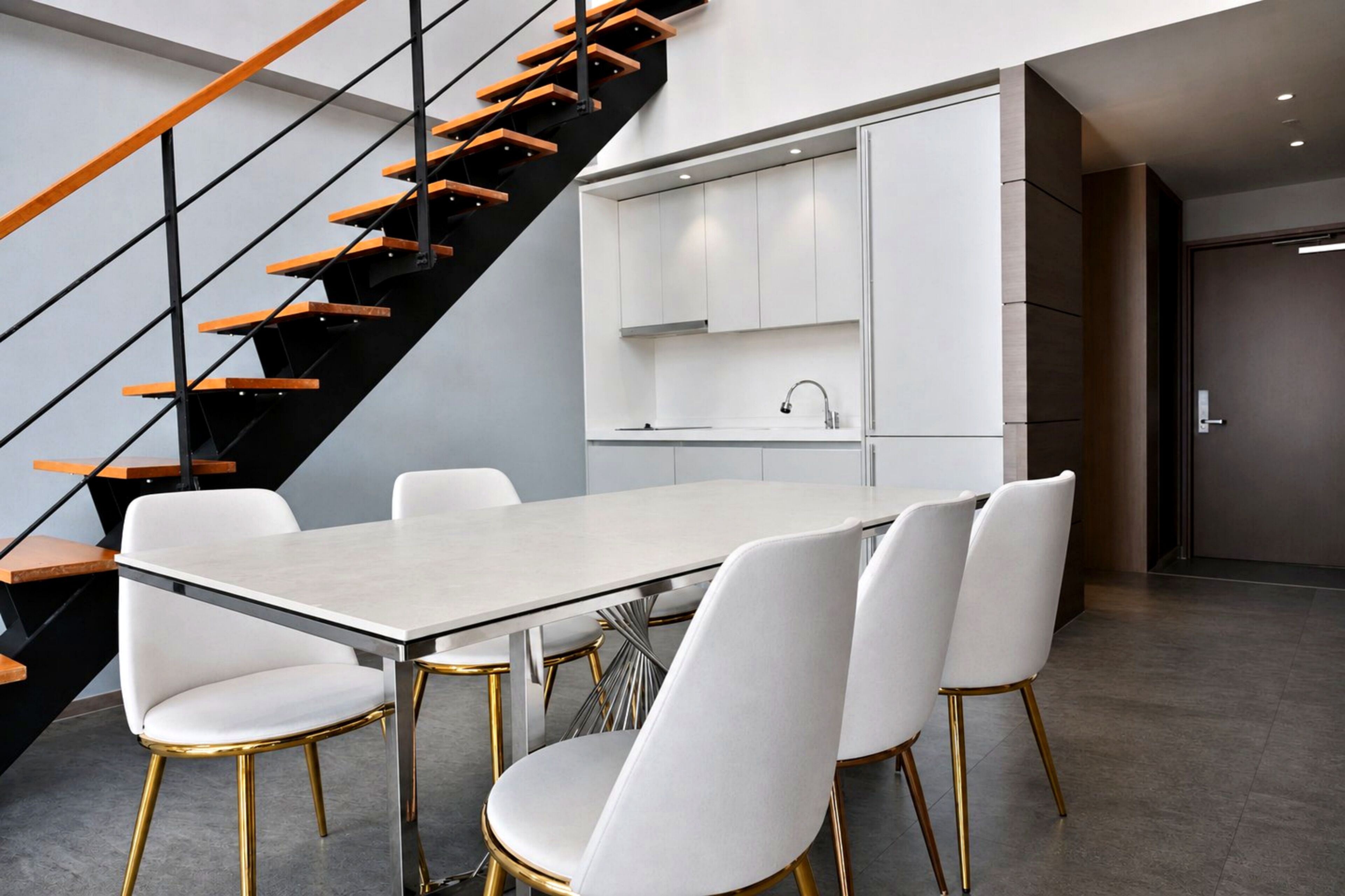 A modern kitchen with white cabinets, a built-in sink, and a staircase with wooden steps.