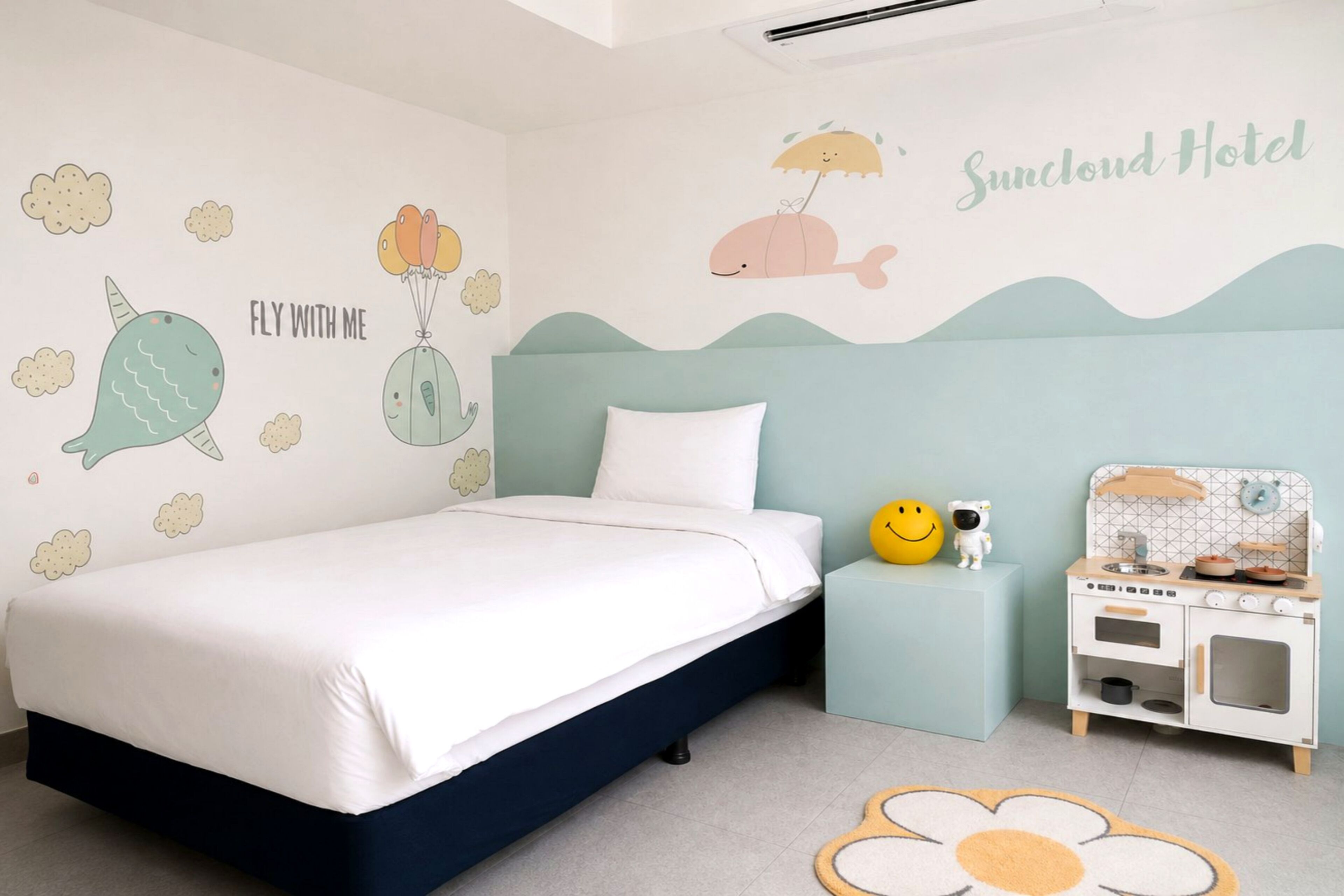 Un dormitorio infantil con una cama, una mesita de noche pequeña y blanca, una cocina de juguete y vinilos decorativos divertidos.