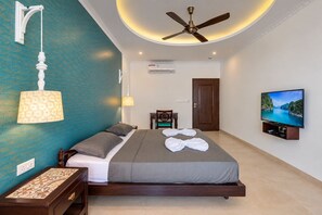 Ein Hotelzimmer mit einem Bett, einem Deckenventilator, einem Fernseher und einer Wandklimaanlage.
