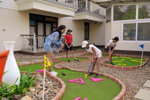 Un campo de mini golf con jugadores, un edificio al fondo y un cielo despejado.