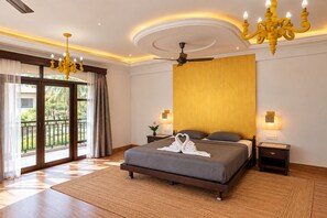 A hotel room with a large bed, a ceiling fan, a chandelier, and a view through the glass doors. - Villa Calangute Phase 17- 12BR + Private Pool + Jacuzzi + Party Room + Games (Calangute)