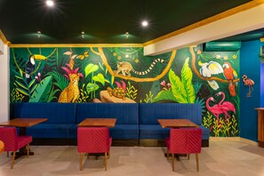 L’intérieur d’un restaurant est décoré d’une fresque représentant la faune de la jungle, avec des sièges bleus et des tables en bois.