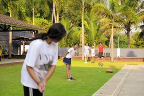 Un grupo de personas jugando golf en un entorno exterior con un césped cuidado y palmeras al fondo.