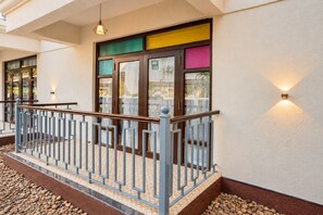 Entrada de hotel con barandilla metálica, un camino empedrado y un diseño de ventana colorido.