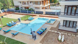 A large rectangular swimming pool with blue lounge chairs around it, a small statue, and a well-maintained garden area.