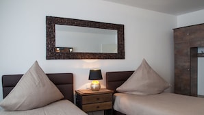 A hotel room with two beds, a nightstand with a lamp, a mirror, and a wardrobe. - Luxusappartement - Die Hotelalternative (Solingen)