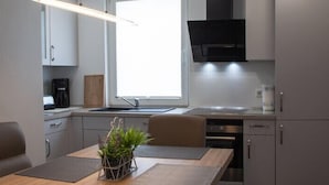 A compact kitchen with a built-in oven, a coffee maker, and a window above the sink. - Luxusappartement - Die Hotelalternative (Solingen)