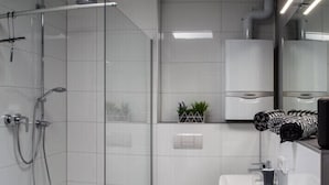 A modern bathroom with a glass shower enclosure, a hairdryer on the counter, and a small plant on the shelf. - Luxusappartement - Die Hotelalternative (Solingen)