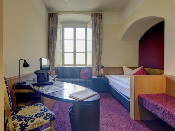 A hotel room with a desk, a sofa, a bed, and a window with curtains. - Klostergasthof Raitenhaslach (Burghausen)