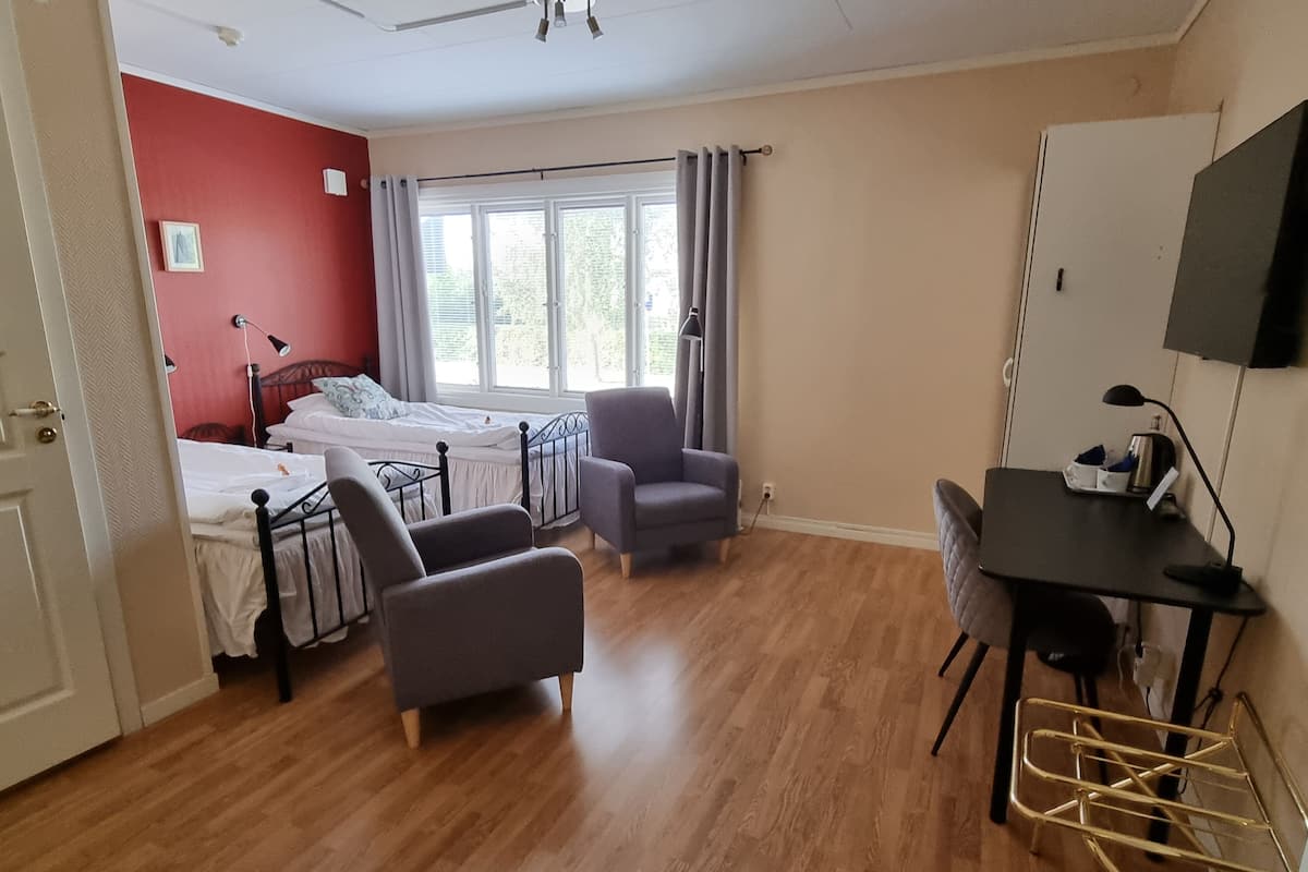A room with a bed, two armchairs, a desk, a television, and a window with curtains.