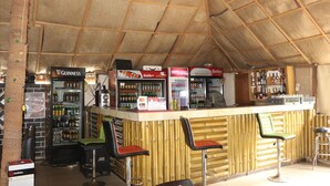 Un espace bar avec un plafond en bois, un comptoir avec des tabourets et des réfrigérateurs remplis de boissons.