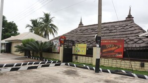 Un bâtiment avec un toit de chaume, une enseigne indiquant « Gula », et un panneau publicitaire faisant la promotion d’un produit pour hommes.
