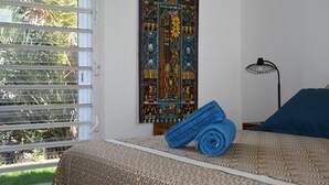 Une chambre à coucher avec un lit, une fenêtre avec des stores, une tapisserie murale et une lampe sur pied.