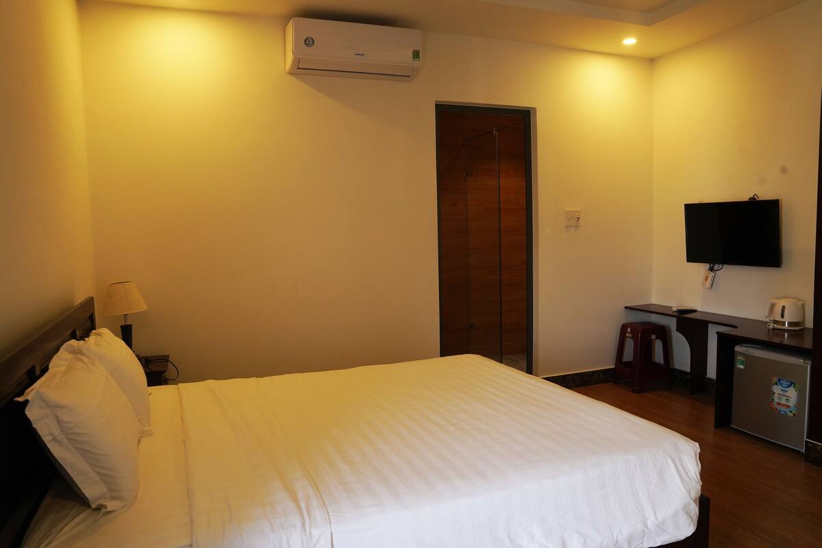 A hotel room with a bed, a desk, a television, and a refrigerator.