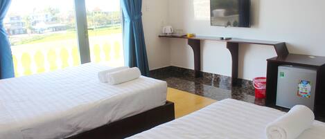A hotel room with two beds, a TV, a small desk, and a window with curtains.
