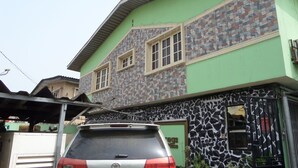 A two-story house with a green facade, a parked silver car, and a stone-patterned wall. - Megsplace Inn (Lagos)