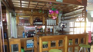 A bar area with wooden stools, shelves stocked with bottles, and a television. - Megsplace Inn (Lagos)