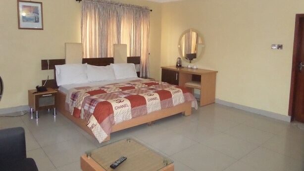 A hotel room with a large bed, a bedside table with a lamp, a small table with a remote control, and a mirror on the wall. - Megsplace Inn (Lagos)